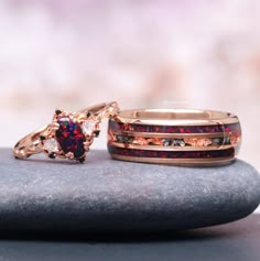 two rings with different colored stones sitting on top of each other next to a rock