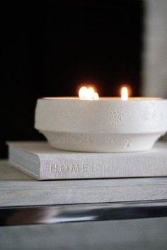 two lit candles sitting in a bowl on top of a book