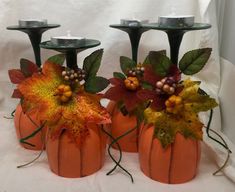 three pumpkins with leaves and berries on them are sitting next to candlesticks