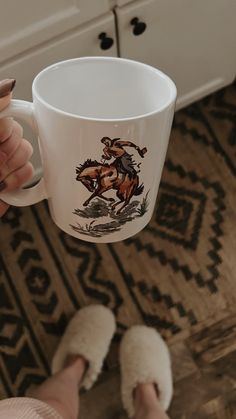 a person holding a coffee cup with a horse on it and slippers in front of them