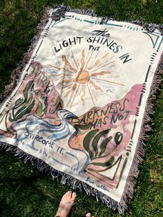 someone is laying on the grass with a blanket that says, light shines in