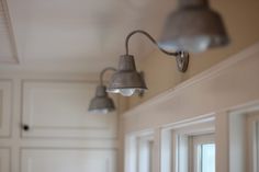 three light fixtures hang from the ceiling in a room with white walls and cabinets behind them