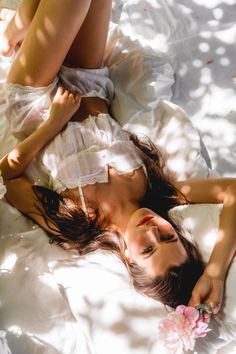 a woman laying on top of a white bed next to a pink flower in her hand