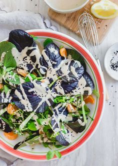 a salad with dressing in a bowl next to a whisk and lemon wedges