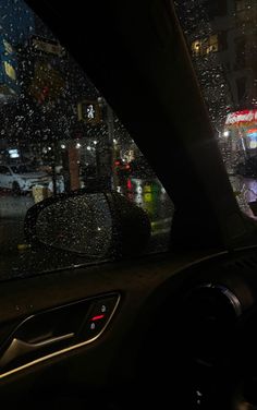 the rain is pouring down on cars in the city at night, with buildings and traffic lights visible through the windshield