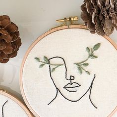 two embroidery hoops with embroidered faces and pine cones