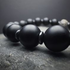 Adorn your wrist with our Men's Onyx Beaded Bracelet, a harmonious fusion of elegance and strength. This gemstone bracelet, featuring meticulously chosen Onyx beads, embodies a minimalist aesthetic that effortlessly complements the modern man's style. The 925 Sterling Silver detailing adds a touch of refinement, ensuring a timeless accessory that stands out. Crafted with a 6 and 8 mm bead arrangement, this stretch bracelet combines the natural allure of Onyx with the comfort of a durable stretch Modern Black Hematite Jewelry, Classic Black Onyx Bracelets, Classic Black Onyx Bracelet, Obsidian Hand-strung Round Beaded Bracelets, Round Onyx Beaded Bracelets With Natural Stones, Black Beaded Bracelets With Spacer Beads, Obsidian Beaded Bracelets With Black Beads, Black Hematite Jewelry With Spacer Beads, Hand-strung Onyx Beaded Bracelets