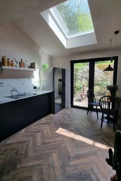 Dark wood herringbone flooring in a kitchen with black cabinets and  white marble topes, there is also  a black and white fridge and a table and chairs to create a dining area. Dark Wood Floors Kitchen, Herringbone Floor Kitchen, Dark Herringbone Floor, Wood Floors Kitchen, Matt Black Kitchen, Vintage Chateau, Antique Wood Floors, Brown Laminate Flooring, Dark Brown Floor