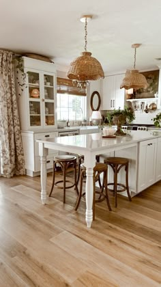 a large kitchen with white cabinets and wooden flooring, two pendant lights hanging over the island