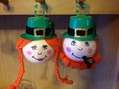 two green hats hanging from hooks on a wooden wall next to a glass filled with liquid