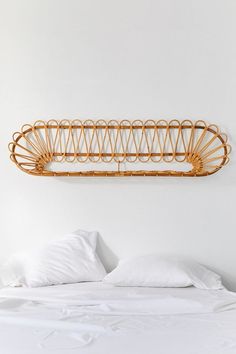 a bed with white sheets and pillows in front of a rattan shelf above the headboard