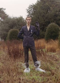 a man standing in the middle of a field wearing a suit and holding his hands up