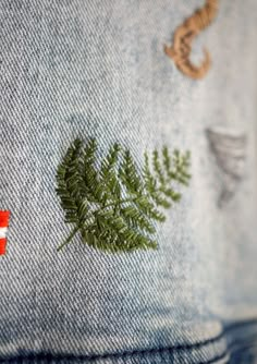 a close up of a pair of jeans with a fern embroidered on the back pocket