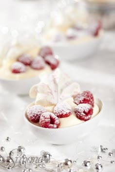 small white bowls filled with desserts covered in powdered sugar and raspberries