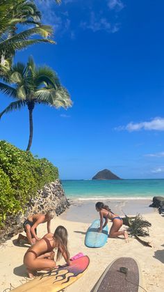 three women in bikinis sitting on the beach with surfboards