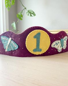 a purple wooden sign with butterflies and a number one on the front, sitting on a table next to a potted plant