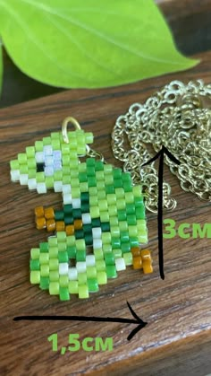 a close up of a piece of jewelry on a wooden table next to a green leaf