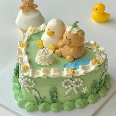 there is a green cake decorated with teddy bears and ducks on the table next to it