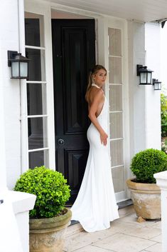 a woman standing in front of a black door wearing a white dress and high heels