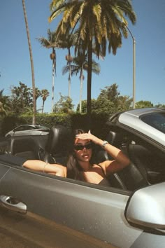 a woman sitting in the driver's seat of a car with palm trees behind her