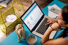 a woman sitting in front of a laptop computer on top of a blue table next to a cup of coffee