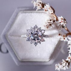 an engagement ring sitting on top of a white box with flowers in front of it