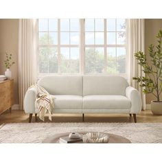 a white couch sitting in front of a window next to a table with a potted plant