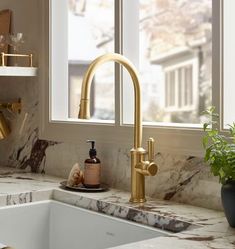 a kitchen sink with gold faucet and marble counter top next to a window