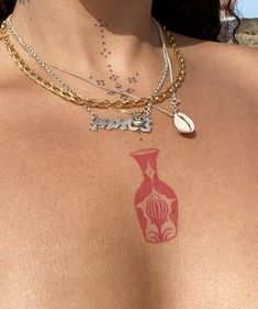 a woman with tattoos on her chest wearing a gold chain and a red vase necklace