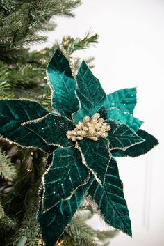 a green christmas ornament hanging from the top of a tree with leaves on it