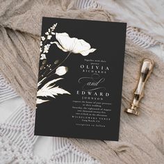 a black and white wedding card with gold foil flowers on it next to a pen