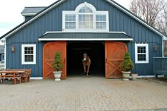 a horse is standing in the doorway of a blue barn with red doors and windows