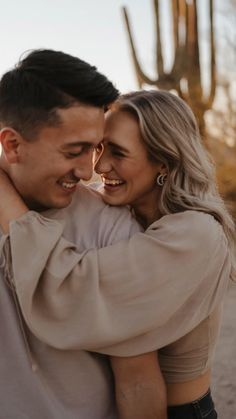 a man and woman embracing each other in front of a cactus plant with the sun shining on them