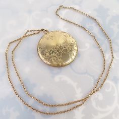 An elaborate engraved foliate design tops this large 1 5/8-inch round Antique gold filled locket. The design was finely carved with flowers, leaves, scrolled lines, a fine straight line sun ray pattern and has a blank area meant for a monogram. The back has a plain shiny gold finish.  The locket opens with a small fingernail groove at the top and closes lightly, but securely. The inside has no frames or inserts, just an old black and white photograph. One side is signed, "D&C" and the locket tested as gold filled (no hallmark). The large pendant hangs from a thick, well-made sturdy vintage gold filled curb chain. It has a nice sheen and true vintage look. The chain stretches 23 1/2 inches and has no clasp. It must be put over the head to wear, so it may not fit everyone. This pairing is in Antique Gold Locket Necklace Stamped 14k, Gold Medallion Locket Necklace Stamped 14k, Antique Medallion Locket Necklace Stamped 14k, Victorian Filigree Locket Necklace In Yellow Gold, Victorian Yellow Gold Locket Necklace With Filigree, Victorian Filigree Yellow Gold Locket Necklace, Gold Etched Victorian Locket Necklace, Antique Yellow Gold Medallion Locket Necklace, Antique Style Yellow Gold Medallion Locket Necklace