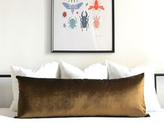 a bed with white sheets and pillows in front of a framed insect print on the wall