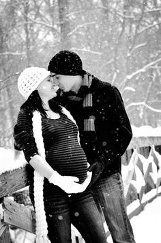 a man and woman standing next to each other on a snow covered bridge with trees in the background