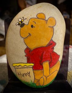 a painted rock with a winnie the pooh holding a honey pot and bee on it