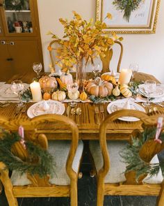 the table is set for thanksgiving dinner with pumpkins and greenery