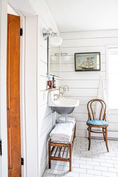 a chair and sink in a white bathroom with wood trim on the wall behind it