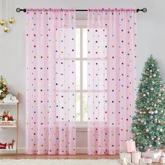 a christmas tree in front of a window with pink curtains and presents on the floor