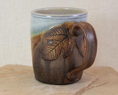 a ceramic mug with leaves on it sitting on top of a stone slab in front of a wall