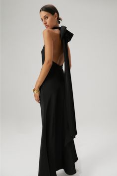 MISHA Evianna Satin Gown in Black. A show-stopping gown for a special someone on their special day. The Evianna Satin maxi dress exudes modern femininity, showcasing high neck and statement back bow detail. - Bias cut skirt- Ruched neckline with buttons at back- Silicone tape around neckline and armholes- Detachable bow and tie- Low scoop back- Invisible centre back zipper Fabric Composition: 100% Polyester Black Maxi Bridesmaid Dress, Modern Black Bridesmaid Dresses, Black Bridesmaid Dresses Black Tie, Gown With Bow At The Back, Long Formal Black Dress, High Neck Low Back Dress, Black Black Tie Dress, Black Bias Cut Dress, Formal Wedding Dresses For Guest