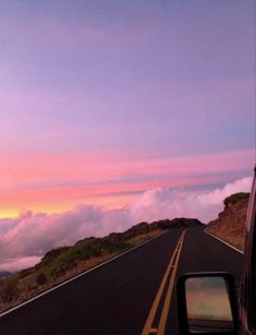 a car driving down the road with clouds in the sky and mountains behind it at sunset