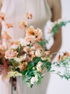 a woman in a white dress holding a bouquet of orange and pink flowers with greenery