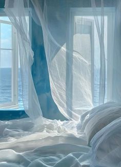 a bed with white sheets and curtains in front of an open window overlooking the ocean