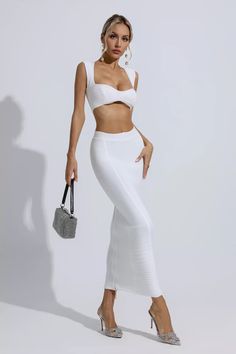 a woman in white is posing with her hand on her hip and holding a purse