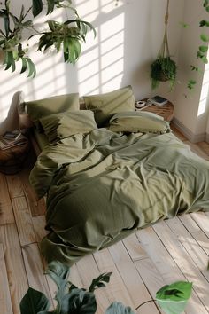 an unmade bed with green sheets and pillows in a room full of plants on the floor