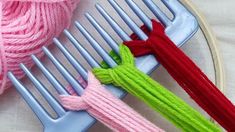 three skeins of yarn sitting on top of a metal comb next to a pink ball of yarn