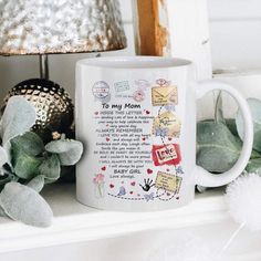 a white coffee mug sitting on top of a shelf next to a plant and a lamp