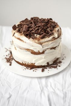 a white plate topped with a cake covered in frosting and chocolate shavings